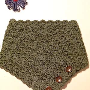 May include: An olive green crocheted cowl with three brown buttons. The cowl features a textured stitch pattern and a scalloped edge. A blue and red decorative flower is in the upper left corner. The item is likely handmade.