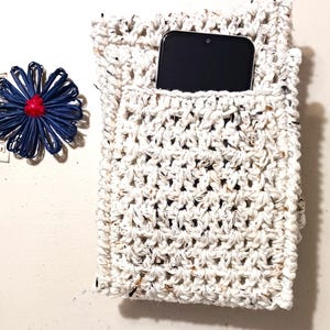 Pode incluir: Uma capa de telefone de croch&ecirc; branca com um smartphone preto dentro. A capa tem um aspecto texturizado e salpicado.