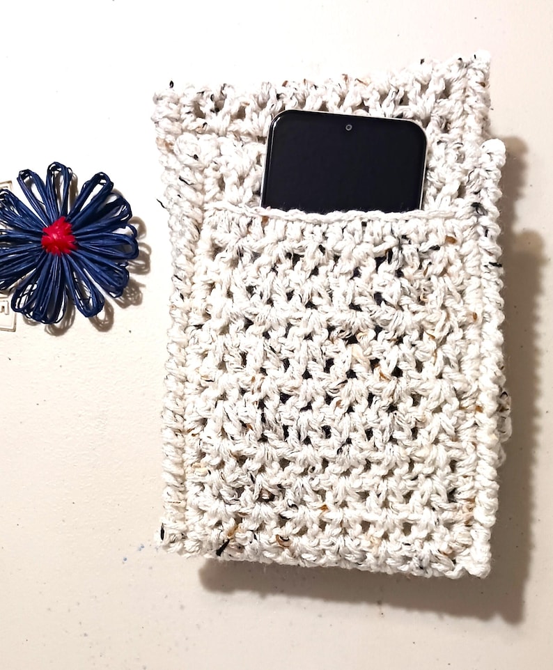 Pode incluir: Uma capa de telefone de croch&ecirc; branca com um smartphone preto dentro. A capa tem um aspecto texturizado e salpicado.