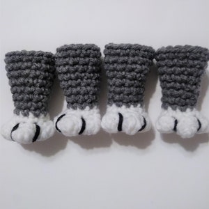 May include: Four crocheted gray and white cat paws with black claws. The paws are arranged in a row on a white surface.