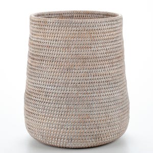 Może przedstawiać: Wysoki, pleciony kosz w jasnobeżowym kolorze. Kosz ma cylindryczny kształt z lekko szerszą podstawą i teksturowaną powierzchnią. Wzór splotu jest widoczny na całej powierzchni.