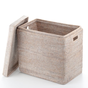 Puede incluir: Una cesta de almacenamiento rectangular tejida con tapa, en color beige natural. La cesta tiene forma rectangular con una tapa parcialmente abierta. La cesta tiene asas en los laterales.