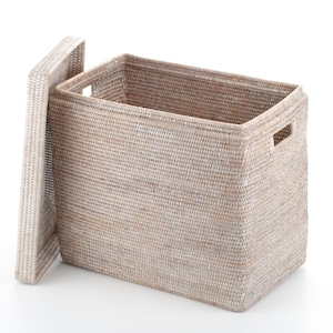 May include: A rectangular woven storage basket with a lid. The basket is light beige with a textured surface and a rectangular opening. The lid is slightly ajar, revealing the interior. The basket has two rectangular handles.