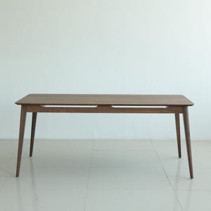 May include: A dark brown wooden dining table with a rectangular top and four slender legs. The table has a unique design with a cutout in the middle of the top.