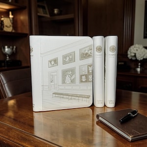 May include: A white binder and three matching book-like items with Japanese text. The binder features a gallery scene with framed artwork. A brown notebook and pen rest on a wooden surface. The items are likely related to the Pokemon franchise.