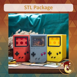 May include: Three handheld game console-shaped card display cases labeled Magic BOY in red, gray, and yellow. The gray case features a central screen area displaying a card, while the red and yellow cases have open screen cutouts. Each case includes a black directional pad and two circular buttons.