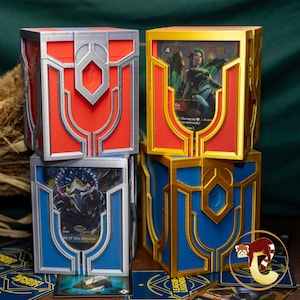 Könnte beinhalten: Vier dekorative Kartenaufbewahrungsboxen in Rot, Blau und Gold mit silbernen Akzenten. Jede Box hat ein einzigartiges Design und fasst Sammelkarten. Die Boxen sind gestapelt, mit sichtbaren Karten im Inneren.