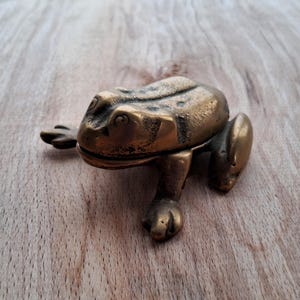May include: A brass frog figurine with a detailed design. The frog is sitting on a wooden surface.