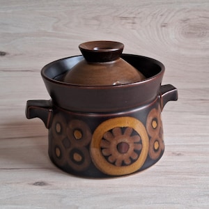 May include: A brown ceramic casserole dish with a lid. The dish has a floral pattern in shades of brown, yellow, and white.