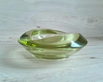 May include: A green glass ashtray with a unique, wavy design. The ashtray is made of clear glass with a green tint.