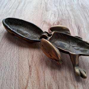 May include: A brass frog-shaped trinket box with a hinged lid. The box is open, revealing the empty interior.