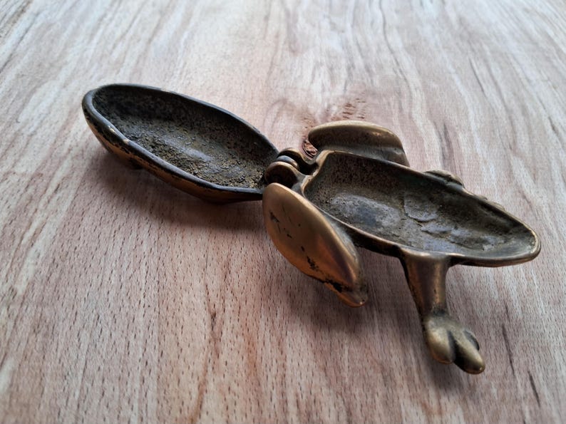 May include: A brass frog-shaped trinket box with a hinged lid. The box is open, revealing the empty interior.