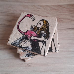 May include: Set of four coasters featuring a pink flamingo and a girl in a white dress. The coasters are made of ceramic and have a rustic, vintage look.