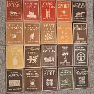 May include: A collection of 20 vintage hardback books with brown, red, and yellow covers. The books are arranged in four rows of five books each. The titles of the books include "Roman Britain", "The English Table", "English Public Schools", "British Sport", "English Novelists", "English Villages", "British Furniture Makers", "Insect Life in Britain", "British Orientalists", "British Statesmen", "Fairs Circuses Music Halls", "The Government of Britain", "English Fashion", "English Popular Traditional Art", "British Universities", "British Drawings", "British Clocks and Clockmakers", "The English Bible", "British Hills and Mountains", and "British Cartoonists Caricaturists and Comic Artists".