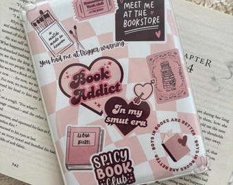 Puede incluir: Una funda de teléfono rosa y blanca con un patrón a cuadros y varias pegatinas. Las pegatinas incluyen un corazón con el texto "Book Addict", un libro con el texto "Slow Burn", un corazón con una flecha y una pegatina que dice "Meet me at the bookstore".