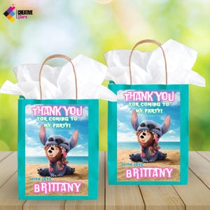 Puede incluir: Dos bolsas de regalo azul turquesa con papel de seda blanco en el interior. Las bolsas tienen una imagen impresa de Stitch de Lilo & Stitch sosteniendo un personaje marr&oacute;n y rosa. El texto en las bolsas dice "&iexcl;Gracias por venir a mi fiesta!" y "Con amor, Brittany".