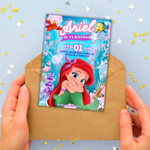 May include: Ariel birthday invitation card featuring the Little Mermaid. The card is held in a brown envelope. The invitation has the text "Ariel is turning 4" and includes the date, time, and location of the party. The card features Ariel, a crab, and a fish.