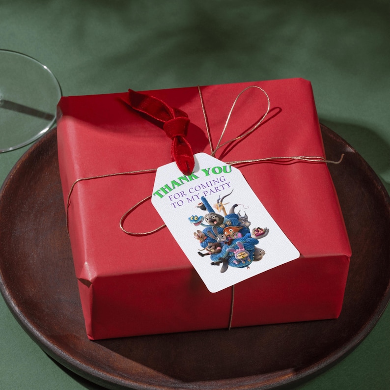 May include: A wrapped red gift box with a red ribbon and a tag that reads "Thank You For Coming To My Party." The tag features a colorful illustration of whimsical characters. The gift is tied with gold twine.
