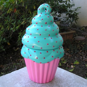 May include: A teal and pink ceramic cupcake cookie jar with a swirl design and pink polka dots.
