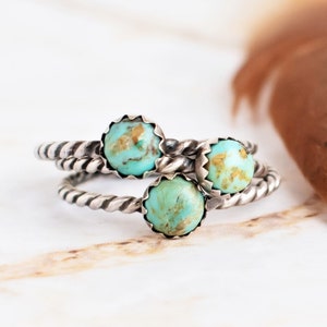 May include: A stackable ring set featuring three round turquoise stones with brown matrix patterns. Each stone is set in a serrated silver bezel atop a twisted rope-style silver band. The rings are arranged to display the stones clearly.