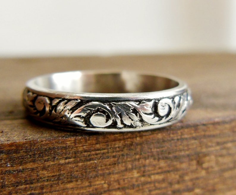 Pode incluir: Um anel de banda de prata com um design floral detalhado gravado em torno de toda a banda.