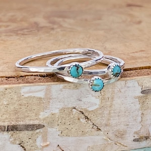 May include: Three silver rings with hammered bands and small turquoise stones. The rings are stacked, showcasing the contrast between the shiny metal and the textured bands. The turquoise stones add a pop of color.