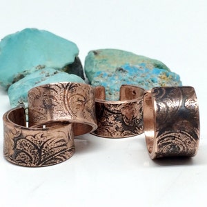May include: Four copper rings with a floral pattern. The rings are stacked on top of each other.