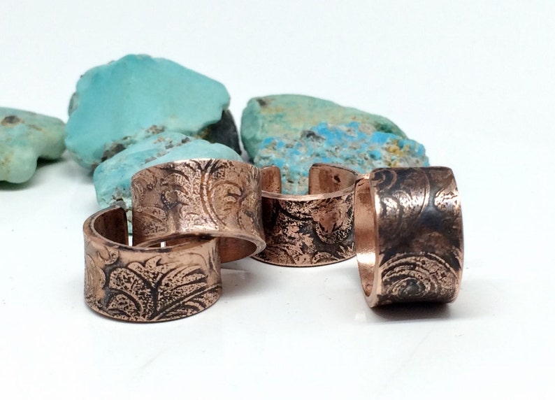 May include: Four copper rings with a floral pattern. The rings are stacked on top of each other.