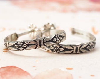 May include: A pair of silver hoop earrings with a floral design. The earrings are simple and elegant, and would make a great gift for any occasion.