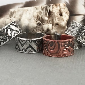 May include: Four silver and copper rings with different engraved designs. The rings are stacked on top of each other.