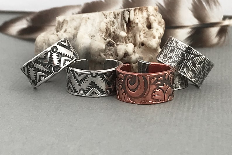 May include: Four silver and copper rings with different engraved designs. The rings are stacked on top of each other.