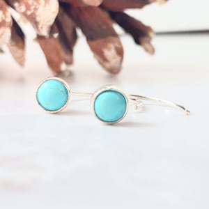 May include: A pair of silver hoop earrings with turquoise stones. The earrings are simple and elegant, and would make a great gift for any occasion.