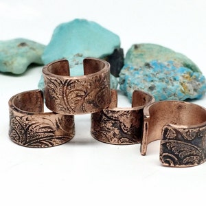 May include: Four copper rings with an ornate floral design. The rings are stacked on top of each other.
