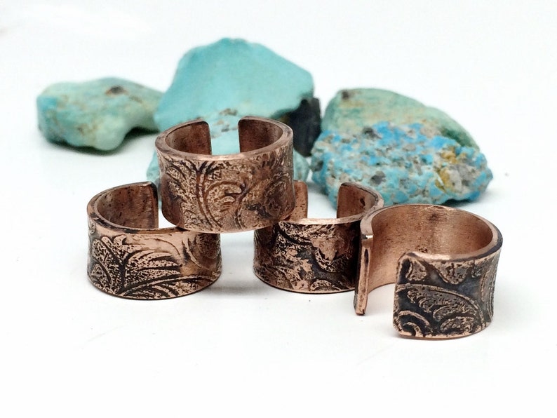 May include: Four copper rings with an ornate floral design. The rings are stacked on top of each other.
