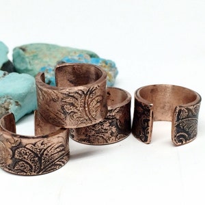 May include: Four copper rings with an ornate floral design. The rings are stacked on top of each other.