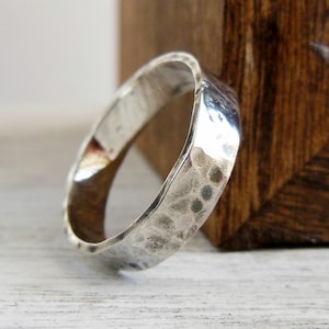 May include: A silver hammered band ring with a textured finish. The ring is wide and has a slightly rounded shape.