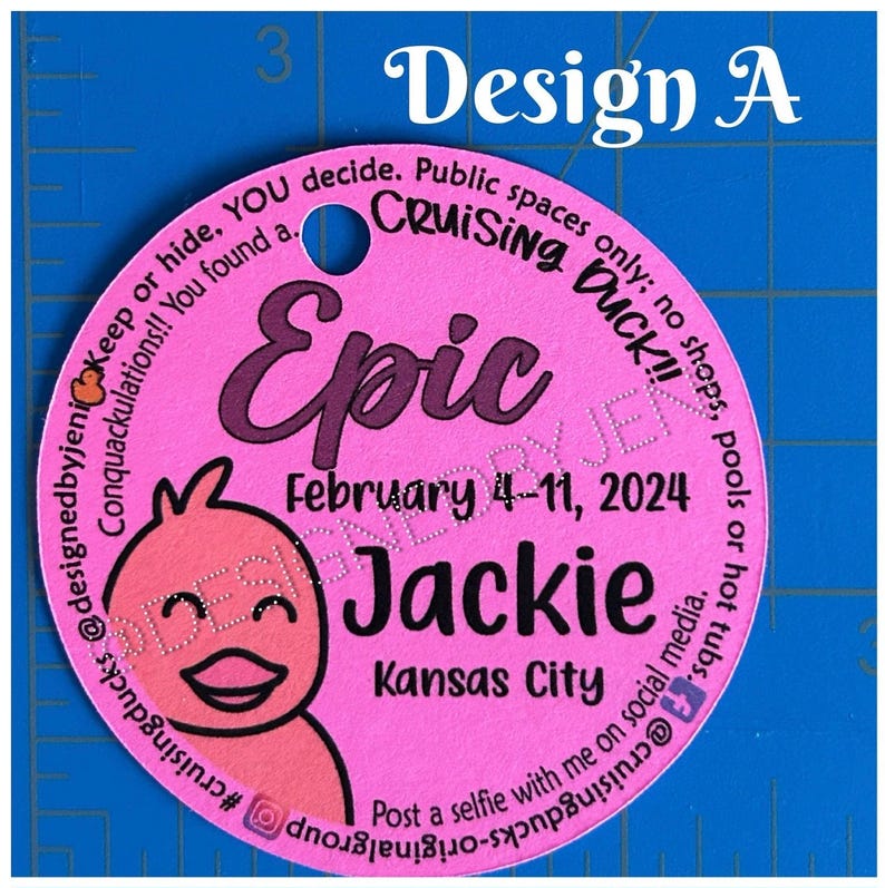 May include: A circular pink tag with a hole at the top, featuring a cartoon duck illustration and black text that reads: Epic, February 4-11, 2024, Jackie, Kansas City, and instructions for cruising ducks, positioned against a blue ruler.