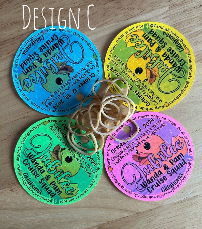 May include: Four circular paper tags in blue, yellow, green, and pink, each featuring a cartoon duck, the text Jubilee, Wanda & Pam Cruise Squad, Oklahoma, and October 12-19, 2024, with a small hole and a cluster of tan rubber bands in the center.