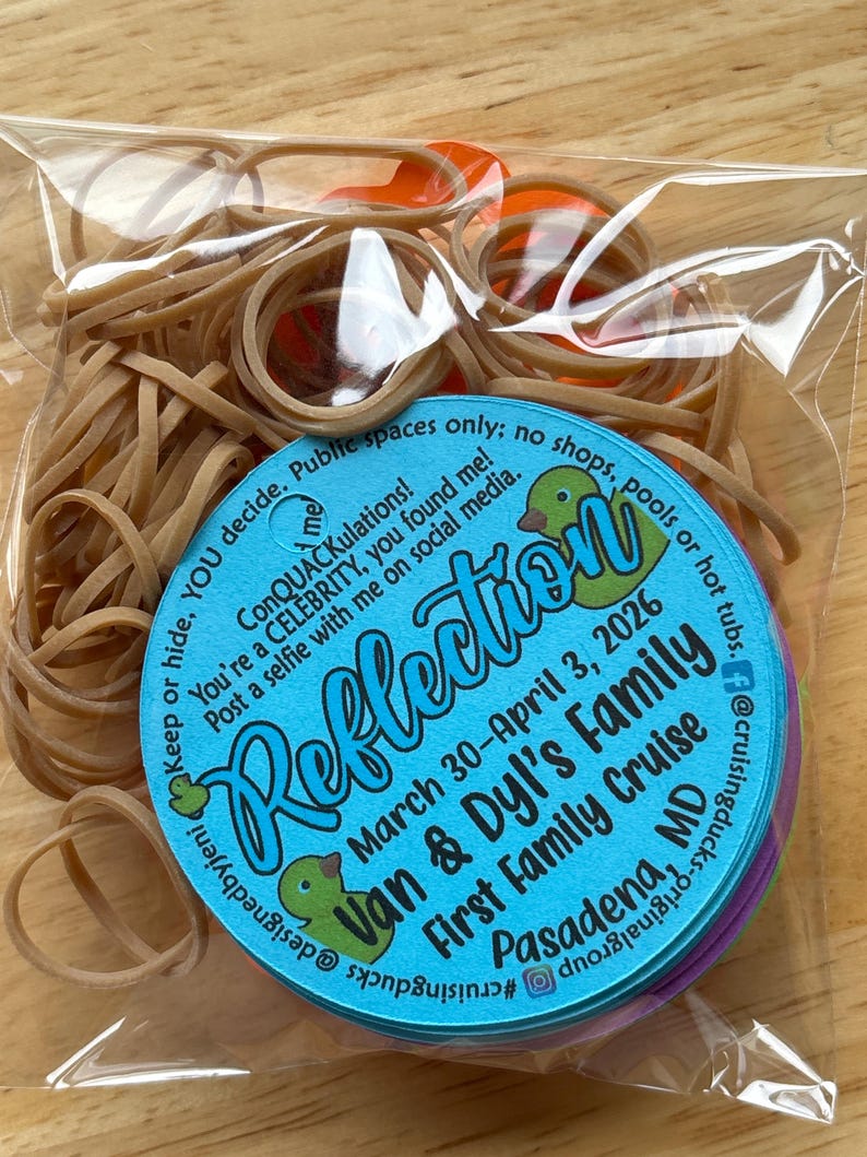 May include: A clear plastic bag filled with tan rubber bands and a round blue tag. The tag features green duck illustrations and text: Reflection, March 30-April 3, 2026, Van & Dyl's Family First Family Cruise, Pasadena, MD, and social media handles.