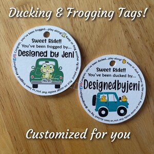 May include: Two round, white, personalized tags with a green truck and a blue jeep. The tags have the text "Sweet Ride!! You've been frogged by... Designed by Jeni" on them. The tags are for a game where players are "frogged" or "ducked".