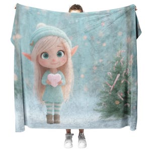 Puede incluir: Una manta azul claro con un elfo de dibujos animados sosteniendo un corazón rosa. El elfo tiene pelo largo y rubio, orejas puntiagudas y lleva un sombrero y un vestido a juego. Un árbol de Navidad con bastones de caramelo está a la derecha.