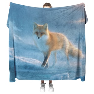 May include: A large, rectangular blanket with a realistic image of a red fox in a snowy scene. The fox has orange fur and white markings, set against a blue and white backdrop. The blanket is being held up by a person.