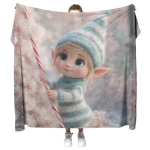Puede incluir: Una manta suave y afelpada con una ilustración caprichosa de un lindo elfo con ojos azules, que lleva un gorro y un suéter a rayas. El elfo sostiene un bastón de caramelo. La manta tiene una paleta de colores claros y pastel.
