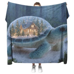 May include: A large blanket with a fantasy design. The design features a turtle with a winter scene inside its shell. The winter scene includes a cabin, snow, and fairy lights. The blanket is held up by a person. The blanket is soft and cozy.