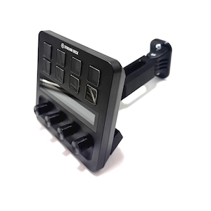 Puede incluir: Dispositivo Stream Deck negro con múltiples botones y perillas. El dispositivo tiene forma rectangular con una pantalla y el texto "STREAM DECK" impreso en la parte superior. Está montado en un soporte negro ajustable.