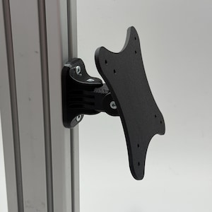 Könnte beinhalten: Ein schwarzer, beweglicher Monitorhalter, der an einer silbernen Metallstütze befestigt ist. Die Halterung verfügt über eine gebogene, perforierte Platte und mehrere verstellbare Gelenke. Die Hardware ist sichtbar und sichert die Halterung an der Stütze. Metrische Maße.