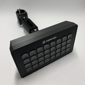 Könnte beinhalten: Ein schwarzes Stream Deck mit 32 anpassbaren Tasten, montiert an einem schwarzen, verstellbaren Arm. Das Stream Deck ist ein Gerät, das für Live-Streaming und Content Creation verwendet wird.