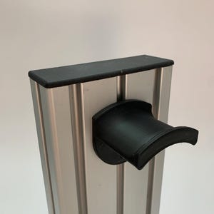 Może przedstawiać: Srebrny metalowy słupek z czarną gumową górą i czarnym zakrzywionym uchwytem przymocowanym z boku. Słupek ma pionowe rowki i jest ustawiony na gładkim białym tle.