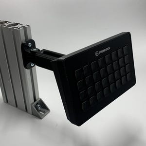 Könnte beinhalten: Ein schwarzes Stream Deck mit 32 anpassbaren Tasten, montiert an einem schwarzen Metallarm, der an einer silbernen Metallhalterung befestigt ist.