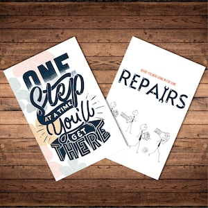 May include: Two white art prints on a wooden surface. One print reads "ONE Step AT A TIME You'll GET THERE" in navy blue and white. The other print says "REPAIRS" with stick figures carrying tools.